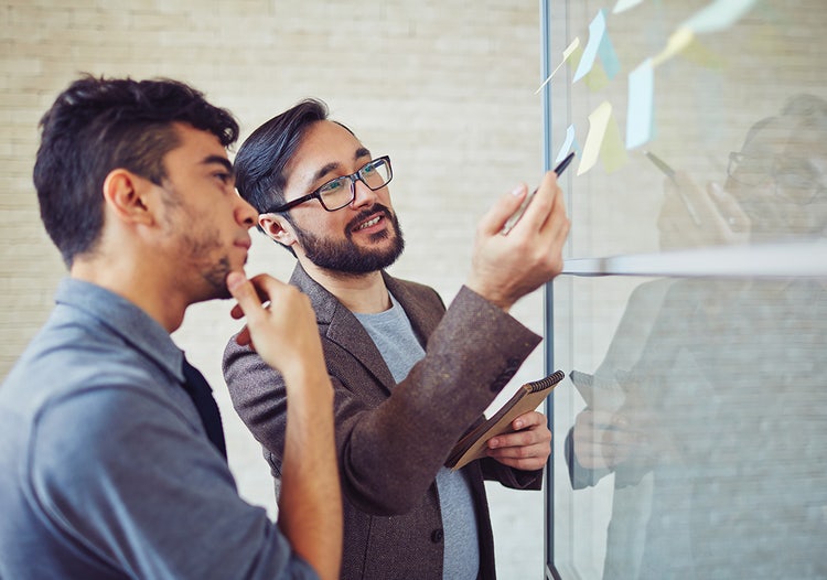 Two people standing next to each other looking at sticky-note papers stuck to a window.