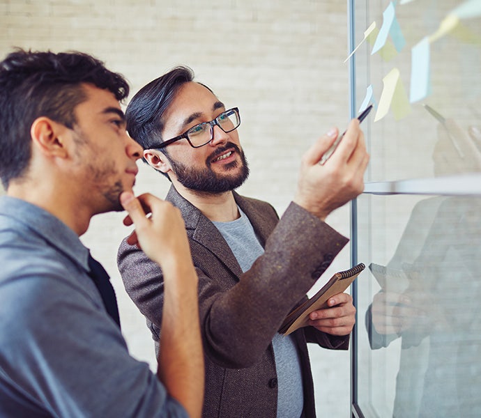 Two people standing next to each other looking at sticky-note papers stuck to a window.